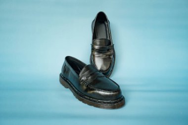 Turkuaz arka planda ayakkabı ustaları tarafından el işçiliğiyle hazırlanmış hakiki sığır derisinden yapılmış tam siyah püsküllü ayakkabıların ayrıntıları.