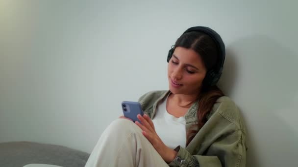 Junges Mädchen ruht sich zu Hause aus, hört Musik über Kopfhörer und singt, während sie auf dem Bett sitzt — Stockvideo
