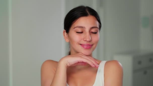 Brunette meisje poseert voor de camera met een glimlach op haar gezicht. Een jong meisje loopt zachtjes haar hand over haar gezicht en kijkt naar de camera — Stockvideo