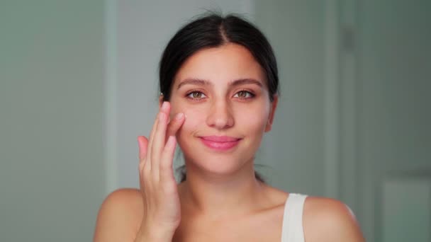 The girl applies the cream to her face with her hand. A young girl smears the cream on her face with her hand. Close-up — Stock Video