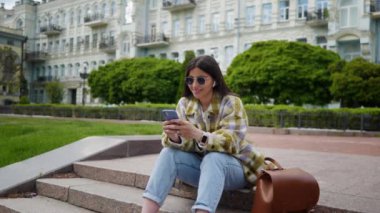 Bir kız sosyal ağlarda yazışıyor. Genç bir kız bir e-postaya cevap verir. Kız, parkta merdivenlerde oturarak ders çalışıyor. Gülümseyen kız doğada dinleniyor ve cep telefonuyla oynuyor.