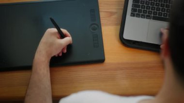 Grafik tabletiyle çalışan bir adam. Web tasarımcısı bir grafik tabletinde çizimler yaratıyor. Bir çalışan grafik tabletine kalemle resim çizer. Ofiste bir dizüstü bilgisayarın başında çalış. Detayları çiziyorum. Yaratıcı