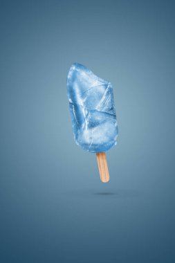 Çubuğun üzerinde dondurmayı ısırdı. Mavi arka planda buzla birlikte fotokopi alanı var. Uçan dondurma. Yaratıcı yaz konsepti. Minimum dondurma konsepti. Yaz havası.