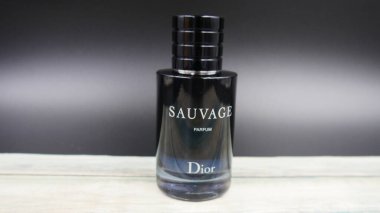 Siyah arka planda Dior Sauvage parfüm şişesi ve ahşap masa.