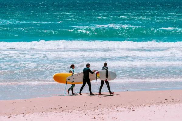 three surfers walking along the beach with the surfboards and chatting