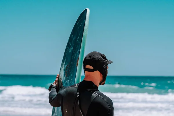 surfer with cap and surfboard looking at the horizon