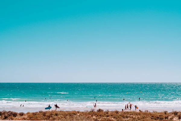 beach crowded with surfers and people sunbathing and playing games.