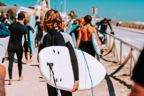 boy with his back to surfboard and walking with his mates