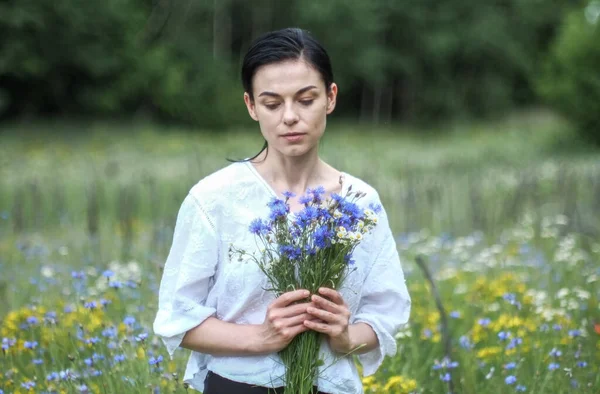 在炎炎夏日的田野里 一位身穿白衣的美丽的乌克兰少女手里拿着野花 — 图库照片