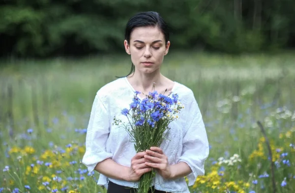 在炎炎夏日的田野里 一位身穿白衣的美丽的乌克兰少女手里拿着野花 — 图库照片