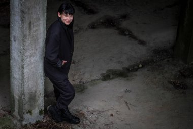 Siyah takım elbiseli güzel bir Ukraynalı genç kız ahşap bir merdivende oturuyor ve terk edilmiş bir fabrikada yürüyor..