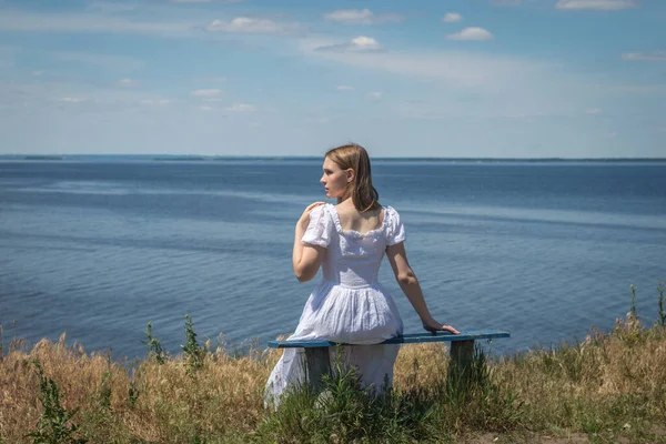 一位身穿白衣的年轻漂亮的乌克兰姑娘正在第聂伯河畔的一条长椅上等着她的男朋友从战场上走出来 — 图库照片