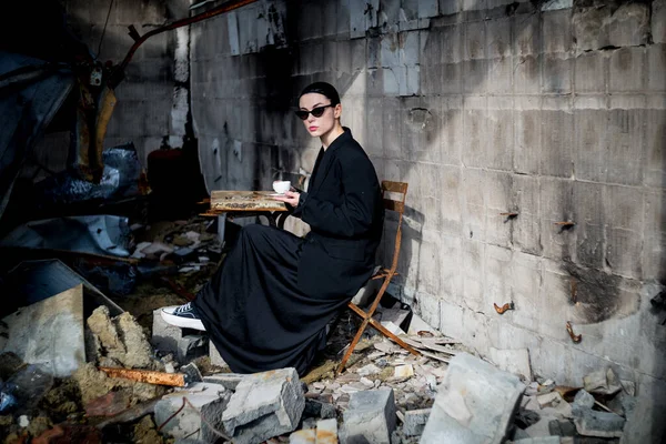 A girl dressed in black is drinking coffee in a destroyed cafe where a Russian army shell hit.