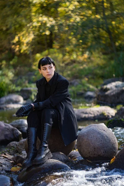 秋天的一天 一个戴着狐狸帽 身穿黑色西服的姑娘出现在河边的花岗岩上 — 图库照片