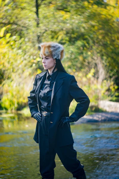 秋天的一天 一个戴着狐狸帽 身穿黑色西服的姑娘出现在河边的花岗岩上 — 图库照片