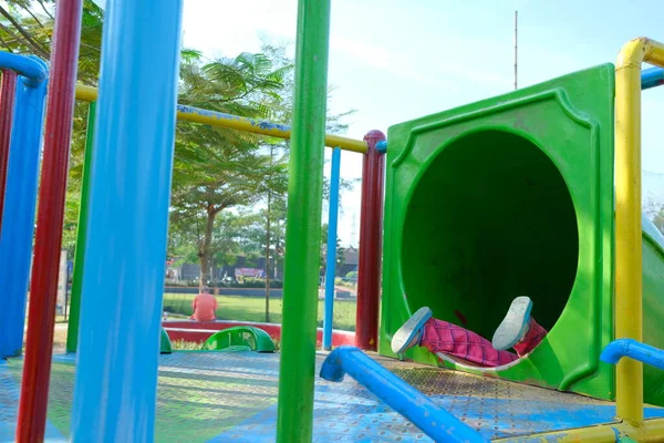 The atmosphere of the playground in the morning, colorful slides, you can see girls\' feet playing on the slide.