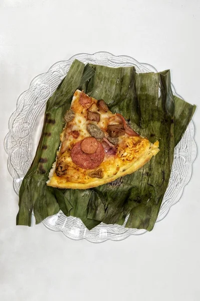 Slice of pizza on a plate with banana leaf and white background.