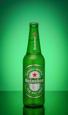 a heineken beer bottle covered with condensation drops on a green glowing background is reflected in a mirror surface