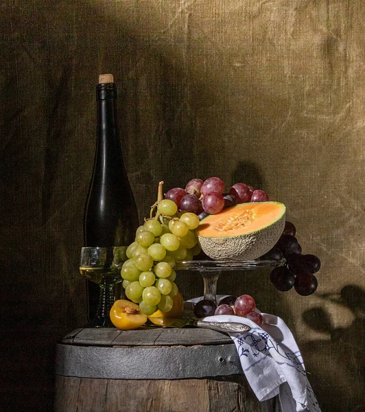 still life of fruit and wine standing on an old wine barrel in a dark basement