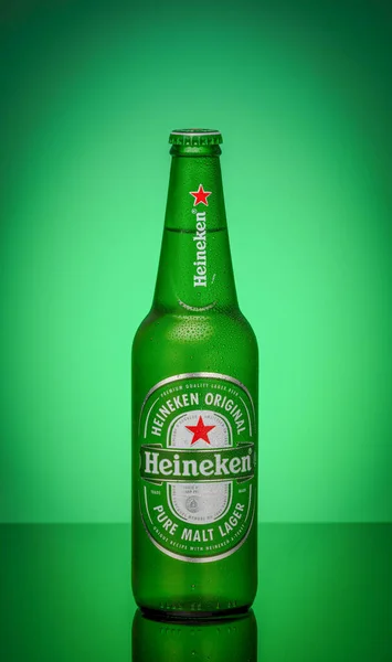 a heineken beer bottle covered with condensation drops on a green glowing background is reflected in a mirror surface