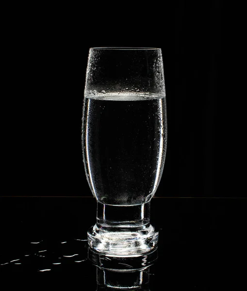 Glass of water on blue background with reflection in the mirror and water splashes.