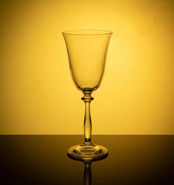 a glass of wine on a glowing orange background is reflected in the mirror surface of the table.