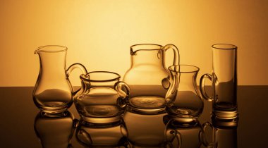 a group of glassware on a luminous orange background is reflected in the mirror surface of the table.