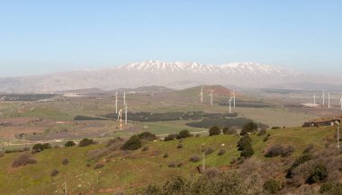 Yakındaki Benthal Dağı 'ndan panoramik bir manzara, yerleşim alanları, tarlalar, rüzgar türbinleri ve kuzey İsrail' deki Golan Tepeleri 'ndeki Hermon Dağı' nın karlı zirvesi.