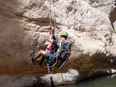 Kudüs, İsrail, Mayıs 05, 2022: Deneyimli bir atlet, genç bir atletin, İsrail 'in Kudüs yakınlarındaki Rathe deresinin suyuna, Yahuda Çölü' nün dağlarına halatla inmesine yardım ediyor..