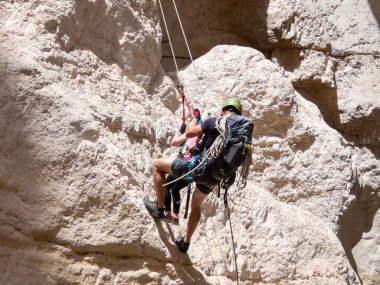 Kudüs, İsrail, Mayıs 05, 2022: Deneyimli bir atlet, İsrail 'in Kudüs yakınlarındaki Rathe deresi yakınlarındaki Judean Çölü' nün dağlarında iple atlamak için ekipman taşıyan genç bir atlete yardım ediyor..
