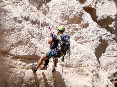 Kudüs, İsrail, Mayıs 05, 2022: Deneyimli bir atlet, İsrail 'in Kudüs yakınlarındaki Rathe deresi yakınlarındaki Judean Çölü' nün dağlarında iple atlamak için ekipman taşıyan genç bir atlete yardım ediyor..