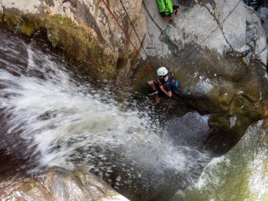 Qatsrin, İsrail, 11 Haziran 2022: Deneyimli bir atlet, İsrail 'in kuzeyindeki Katsrin yakınlarındaki Golan Tepeleri' ndeki Zavitan deresinin kıyısındaki Kara Geçit 'teki bir şelaleye halatla atlamak için ekipmanla birlikte iniyor.