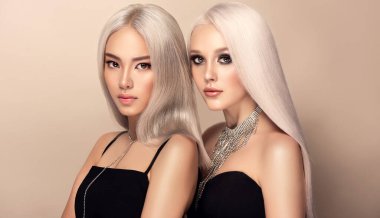 İki beyaz elbiseli, saçları aşırı sarışına boyanmış güzel kadın. Güzellik salonunda şık kız saç stili bukleleri. Moda, kozmetik ve makyaj.