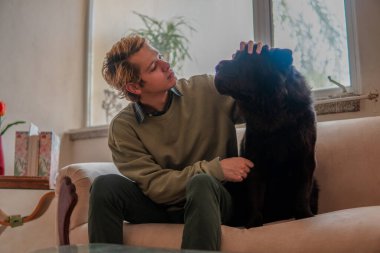 Çocuk oturma odasındaki kanepede oturan evcil hayvanını okşuyor ve gözlemliyor..