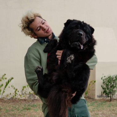 Sarışın çocuk büyük siyah köpeğini komik bir şekilde taşıyor.