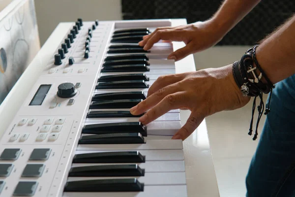 Two hands of a man playing the keyboard in a studio. Professional studio with a keyboard. Two hands are touching a keyboard. Abrazalet on the left hand.