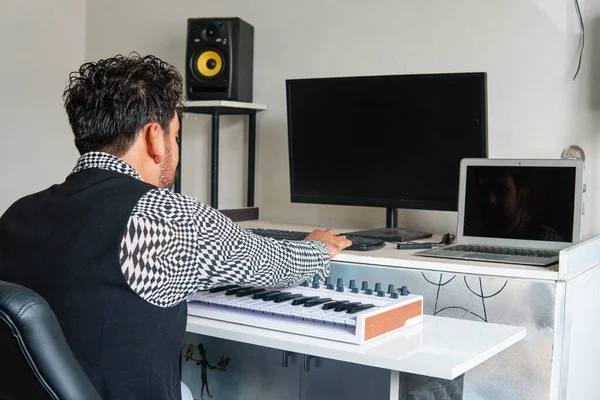 Music producer working in his studio with his computer, laptop, keyboard, and microphone. White room with music producer equipment. Recording and editing music studio. Producer of music dressed with
