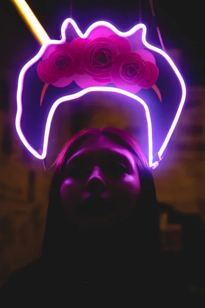 Woman with a neon light crown. A girl on a black background is illuminated by intense pink light. Frida Kahlo with intense neon light. Girl about neon lights.