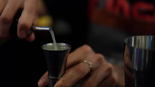 A bartender serves liquid to a shaker to prepare a drink. Close-up of bartender instruments. Hands of bartender preparing a drink. Bartender mixing to prepare a drink.