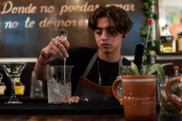 Waiter preparing a drink mixing with a shaker. Bartender at the bar counter preparing a drink. Waiter cooling glass with ice. Small pot on the bar counter.