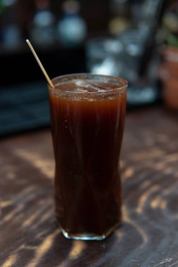 Bir barın karanlık arka planında iç. Bar tezgahında ahşap karıştırıcı ile alkollü içecek. Bir gece kulübü içkisine ne dersin?.