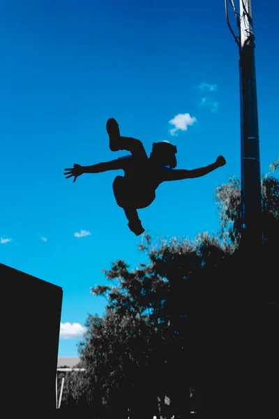 Black silhouette of a man in the middle of a cartwheel. Parkour athlete practicing. Dark silhouette of a spin in the air of an acrobat. Unrecognizable gymnast practicing his turns outdoors.