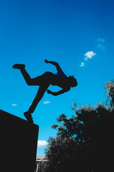 Black silhouette of an unrecognizable man practicing parkour. Man with the sky in the background doing a somersault. Man in the air in the middle of a stunt. Black silhouette of athlete man.