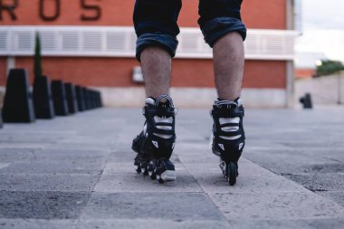 Pair of roller skates on the street rolling. Boy walking with his black roller skates. Skates seen from behind. Skates rolling on an esplanade. High quality photo