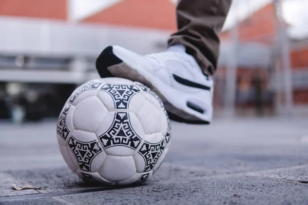 Soccer ball with one foot stopping it. Close up of a black and white soccer ball. White tennis and a white ball. High quality photo. Boy playing soccer in the street