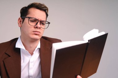 Man with brown suit and glasses elegantly dressed. Business man reading a black book on a white background. Elegant man on white background reading. Confused man reading. High quality photo