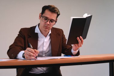 Man working at his desk. Business executive dressed in a suit wearing glasses and holding a black notepad. Business man working while signing papers. High quality photo