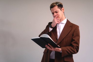 Elegant man with thoughtful expression while reading a book. Business man reading on a white background. Caucasian man dressed in brown suit and white shirt. Lawyer reading worried.