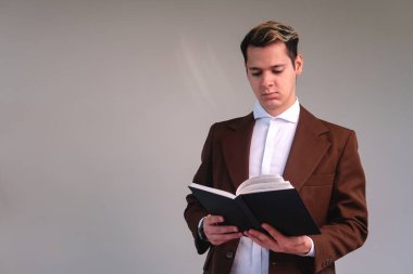 Concentrated businessman reading a book on a white background. Elegant man in a suit on an isolated white background. Caucasian male teacher reading his black notebook while he lectures.