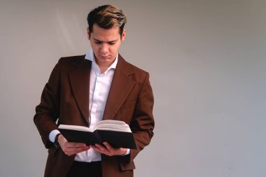 Caucasian blond man elegantly dressed in a suit, shirt and a watch reading a book on a white background. Business man reading. Teacher on a white isolated background reading.